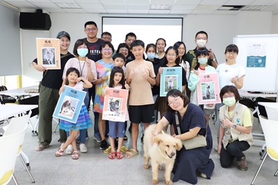 《與動物相愛的練習︱狗狗的家人時光遊戲課》學員與待認養狗狗溫馨合影，手舉認養犬隻的介紹牌。